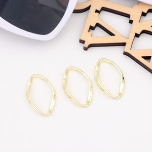 Puede incluir: Tres anillos de metal de color dorado con una forma ondulada irregular. Los anillos están sobre una superficie blanca.