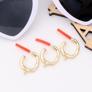 May include: Three gold hoop earrings with a textured, irregular surface. Each earring has a red plastic post.
