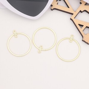 May include: Three gold-coloured metal hoops with a small loop on each side. The hoops are different sizes and are arranged in a row on a white surface.