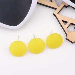 May include: Three yellow round earrings with silver posts. The earrings are on a white surface.