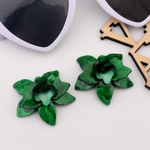 Puede incluir: Un par de pendientes verdes con forma de flor. Los pendientes están hechos de un material brillante y marmoleado.