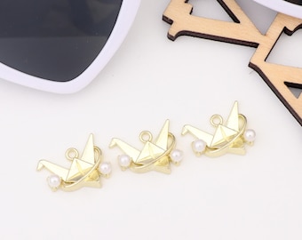 Peut inclure: Trois breloques en or en forme de grue origami avec des accents de perles blanches. Chaque breloque présente un délicat motif de grue origami avec une perle sur chaque côté de la grue.