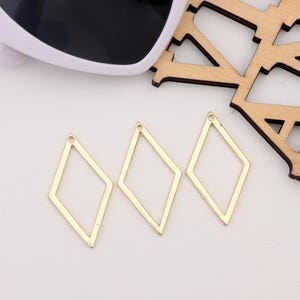 Puede incluir: Tres dijes de metal de forma de diamante de color dorado con un pequeño agujero en la parte superior para sujetar a joyas u otras artesanías.