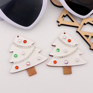 May include: Two white wooden Christmas tree decorations with red, green and iridescent rhinestones, white pearl beads and silver glitter.