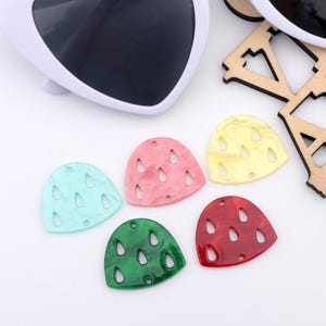 Könnte beinhalten: Fünf bunte Plastik-Wassermelonen-Scheibenformen mit ausgeschnittenen Details. Die Formen sind in Rot, Grün, Gelb, Rosa und Hellblau.