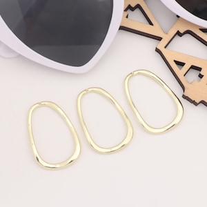 May include: Three gold-colored, irregular oval-shaped hoops. The hoops are smooth and have a slightly hammered texture.