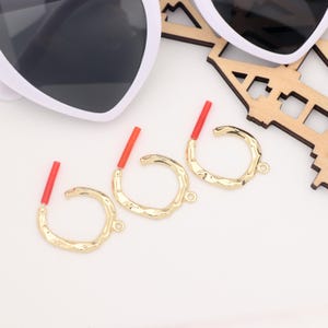 May include: Three gold hoop earrings with a textured finish and red accents. The earrings are on a white surface.