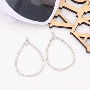 Puede incluir: Dos blanks de pendientes de plata en forma de lágrima con una superficie texturizada. Cada blank tiene un pequeño bucle en la parte superior para sujetar los hilos de los pendientes.