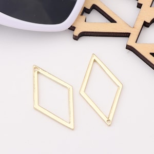 Op de afbeelding: Twee gouden metalen hangers in de vorm van een diamant met een klein gaatje bovenaan om aan sieraden te bevestigen.