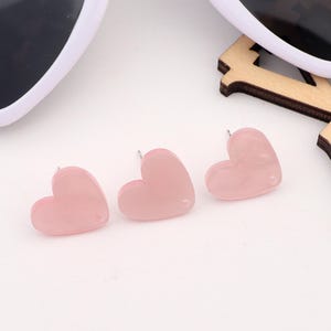 May include: Three pink heart-shaped stud earrings. The earrings are made of a translucent material with a slightly marbled effect.