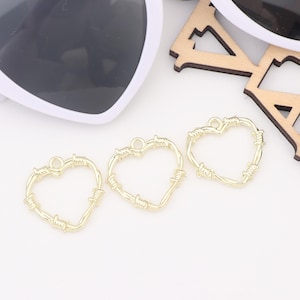 May include: Three gold-colored heart-shaped charms with a barbed wire design. The charms are perfect for adding a unique touch to jewelry projects.
