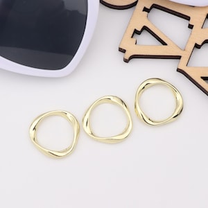 May include: Three gold-colored metal rings with a wavy, irregular shape. The rings are arranged in a row on a white surface.
