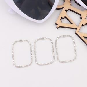 May include: Three silver square-shaped metal frames with a textured finish. The frames have a small loop at the top.