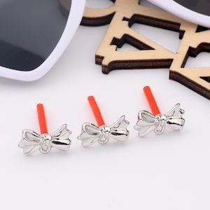May include: Three silver bow-shaped charms with red stems. The charms are small and delicate, and they would be perfect for adding a touch of whimsy to jewelry or other crafts.