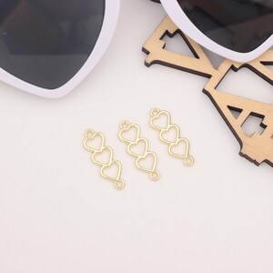 May include: Three gold-colored metal charms, each featuring three connected heart shapes. The hearts are hollow and have a smooth, polished finish.