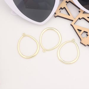 May include: Three gold-coloured metal oval-shaped pendant blanks with a small loop at the top.