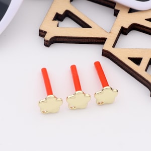 May include: Three gold flower-shaped charms with red posts. The charms are about 1 cm in diameter.