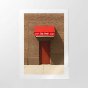 Peut inclure: Une auvent rouge avec le texte "Cine Magic East Village Studio's" au-dessus d'une porte rouge avec un mur de briques en arrière-plan.