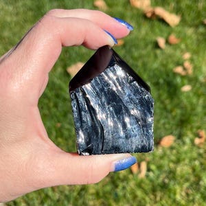 May include: A black obsidian crystal with a unique, striated pattern. The crystal is shaped like a house and has a reflective surface.