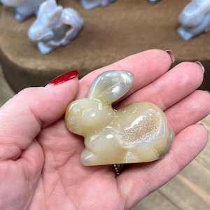 May include: A small, white agate rabbit figurine with a detailed, textured surface. The rabbit is sitting on its hind legs with its ears perked up.