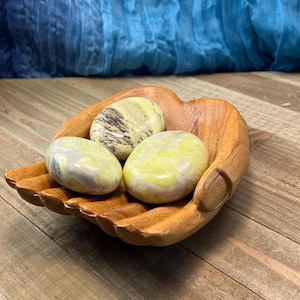 May include: Three smooth, polished green and white stones in a wooden hand-shaped bowl. The stones are a light green with white and gray swirls.