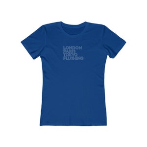 May include: A royal blue t-shirt with the words "LONDON PARIS TOKYO FLUSHING" printed in a light blue font. The text is stacked vertically. The shirt has short sleeves and a crew neck.
