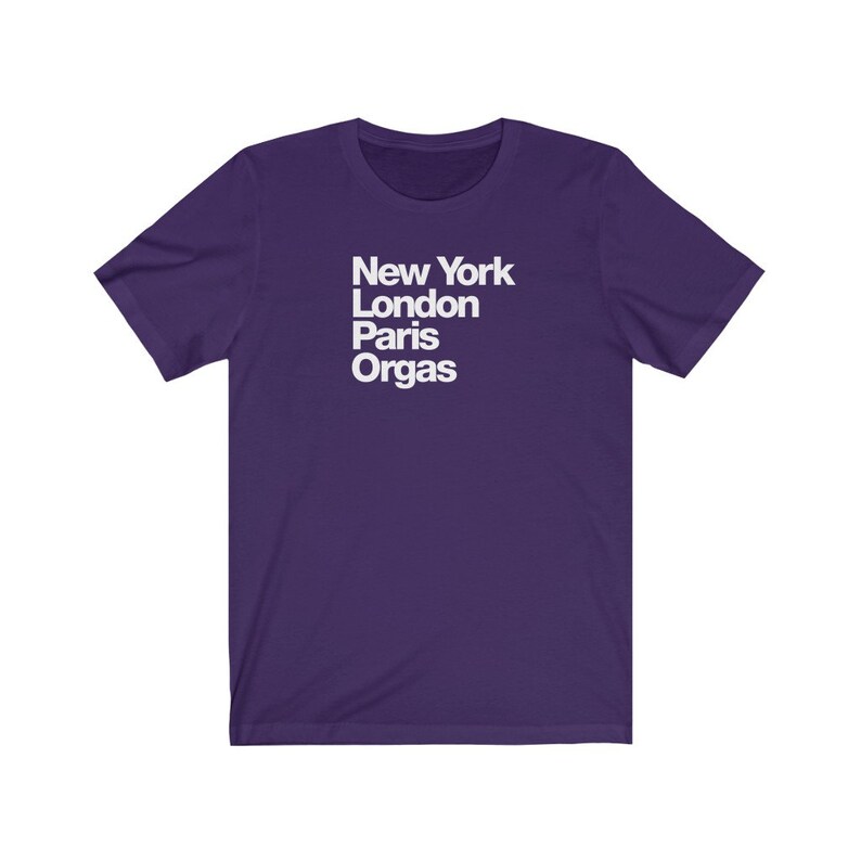 Puede incluir: Camiseta de manga corta de color morado con texto blanco que dice "New York London Paris Orgas".