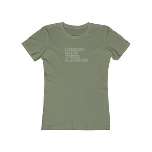 May include: Olive green t-shirt with the words "LONDON PARIS TOKYO FLATBUSH" printed in white, stacked vertically. The shirt has short sleeves and a crew neck.