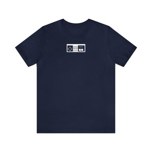 Puede incluir: Una camiseta azul marino con un gráfico blanco de un mando de consola de videojuegos clásico.