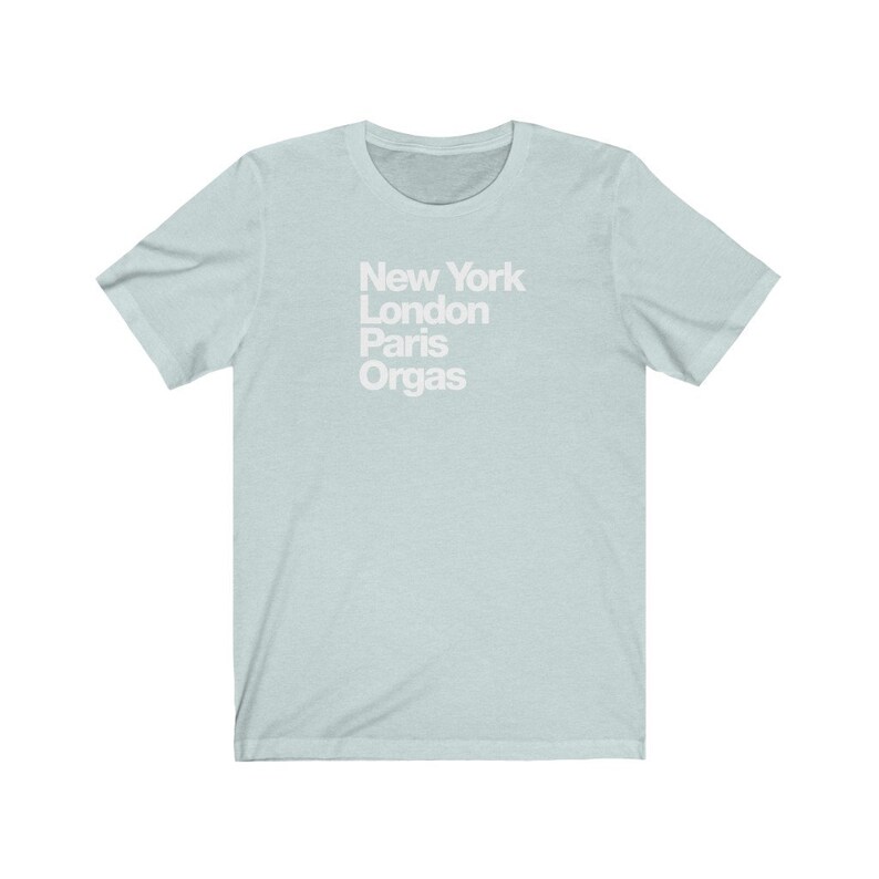 Puede incluir: Una camiseta azul claro con el texto "New York London Paris Orgas" impreso en blanco en la parte delantera.