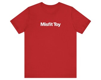 May include: A red t-shirt with the white text "Misfit Toy" centered on the front. The short-sleeved shirt is made of a soft material and is suitable for casual wear. The shirt is a solid red color.