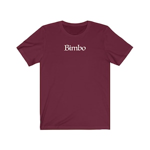 Könnte beinhalten: Ein kurzärmeliges T-Shirt in der Farbe Weinrot mit dem Wort "Bimbo" in weiß auf der Vorderseite.