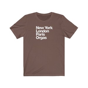 Puede incluir: Una camiseta marr&oacute;n con texto blanco que dice "New York London Paris Orgas"