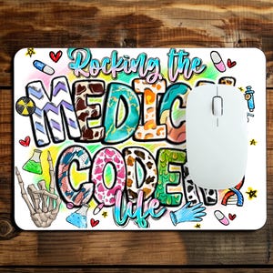 Op de afbeelding: Een rechthoekige muismat met de tekst "Rocking the MEDICAL CODER life" in kleurrijke, gedessineerde blokletters. Het ontwerp bevat illustraties van pillen, een skeletthand, een DNA-streng, een injectiespuit en laboratoriumbekers.