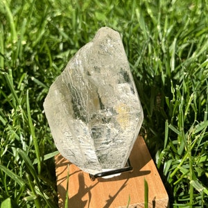 May include: A clear, faceted crystal on a wooden stand. The crystal is sitting on a bed of green grass.