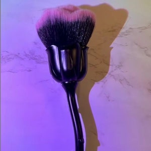 Może przedstawiać: Czarny pędzel do makijażu z uchwytem w kształcie róży i różowymi włosiem.