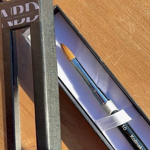 Może przedstawiać: Czarny i srebrny pędzel do zdobienia paznokci z etykietą Kolinsky i numerem 10. Pędzel znajduje się w czarnym pudełku z białym wnętrzem.