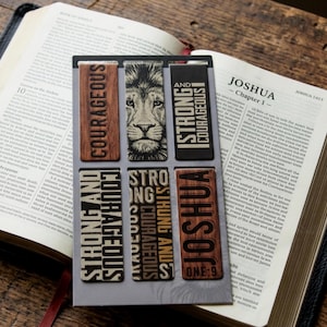 May include: A set of six rectangular bookmarks with inspirational text and a lion's face. The bookmarks feature phrases like "Courageous" and "Strong and Courageous" in a mix of fonts and colors, set against wood grain and black backgrounds.