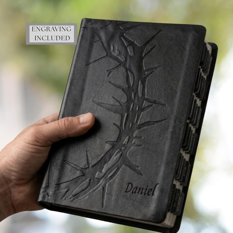 May include: Black leather-bound book with embossed thorn design and the name "Daniel" in script. The book has labeled page dividers and the text "ENGRAVING INCLUDED" in a gray box.