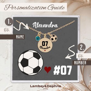 K&ouml;nnte beinhalten: Eine goldene Halskette mit einem Fu&szlig;ball-Anh&auml;nger, einem blauen Kristall-Anh&auml;nger und einem runden Anh&auml;nger mit der Nummer 07 und dem Namen Alexandra. Die Halskette befindet sich in einer wei&szlig;en Schachtel mit grauem Hintergrund und dem Text "Personalisierungsleitfaden" oben. Der Text "An: NAME" befindet sich auf der linken Seite der Schachtel und der Text "An: NUMMER" auf der rechten Seite der Schachtel.