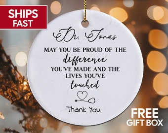 Puede incluir: Adorno de cerámica blanca con un patrón de mármol que presenta el texto "Dr. Jonas May you be proud of the difference you've made and the lives you've touched" con un estetoscopio y un símbolo de corazón. El texto "Thank You" está debajo del símbolo.