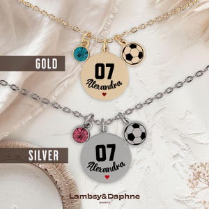 K&ouml;nnte beinhalten: Zwei Halsketten mit einem Fu&szlig;ball-Anh&auml;nger, einem Kristall-Anh&auml;nger und einem runden Anh&auml;nger mit der Nummer 07 und dem Namen Alexandra. Die obere Halskette ist golden und die untere Halskette ist silber.
