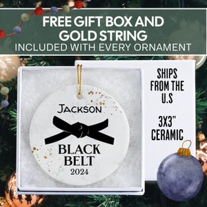 May include: White ceramic Christmas ornament with a black belt design and the text "JACKSON BLACK BELT 2024".
