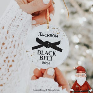May include: White round Christmas ornament with a black belt design and the text "Jackson Black Belt 2024".