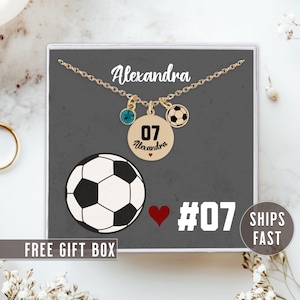 K&ouml;nnte beinhalten: Goldkette mit einem Fu&szlig;ball-Anh&auml;nger, einem blauen Kristall-Anh&auml;nger und einem runden Anh&auml;nger mit der Nummer 07 und dem Namen Alexandra. Die Kette befindet sich in einer grauen Schachtel mit dem Text "FREE GIFT BOX" und "SHIPS FAST".