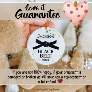 May include: White ceramic Christmas ornament with gold flecks, featuring a black belt with the text "JACKSON BLACK BELT 2024".