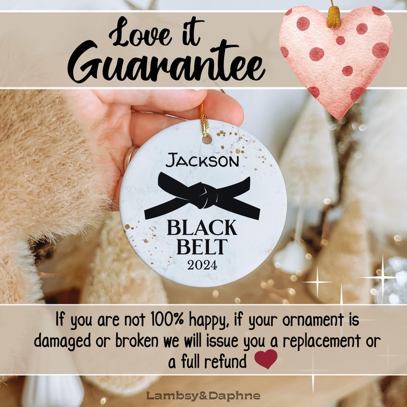 May include: White ceramic Christmas ornament with gold flecks, featuring a black belt with the text "JACKSON BLACK BELT 2024".
