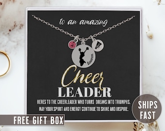 Pode incluir: Um colar de prata com um pingente de uma silhueta de líder de torcida, um strass rosa e um pingente de megafone prateado. O colar está em uma caixa preta com o texto "to an amazing Cheer LEADER" e "HERES TO THE CHEERLEADER WHO TURNS DREAMS INTO TRIUMPHS. MAY YOUR SPIRIT AND ENERGY CONTINUE TO SHINE AND INSPIRE." A caixa também tem o texto "SHIPS FAST" e "FREE GIFT BOX".