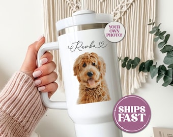 May include: White travel mug featuring a custom pet portrait of a golden doodle dog. The mug has a handle and a lid. The dog's name, "Ramba", is written in cursive above the image. A circular sticker says "Your Own Photo!"