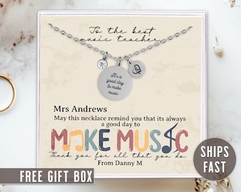 May include: A silver necklace with a charm that says "It's a good day to make music" and a charm with a heart and the letter "B". The necklace is in a white box with a message that says "To the best music teacher" and "Make Music". The box also says "Mrs. Andrews" and "Thank you for all that you do. From Danny M".